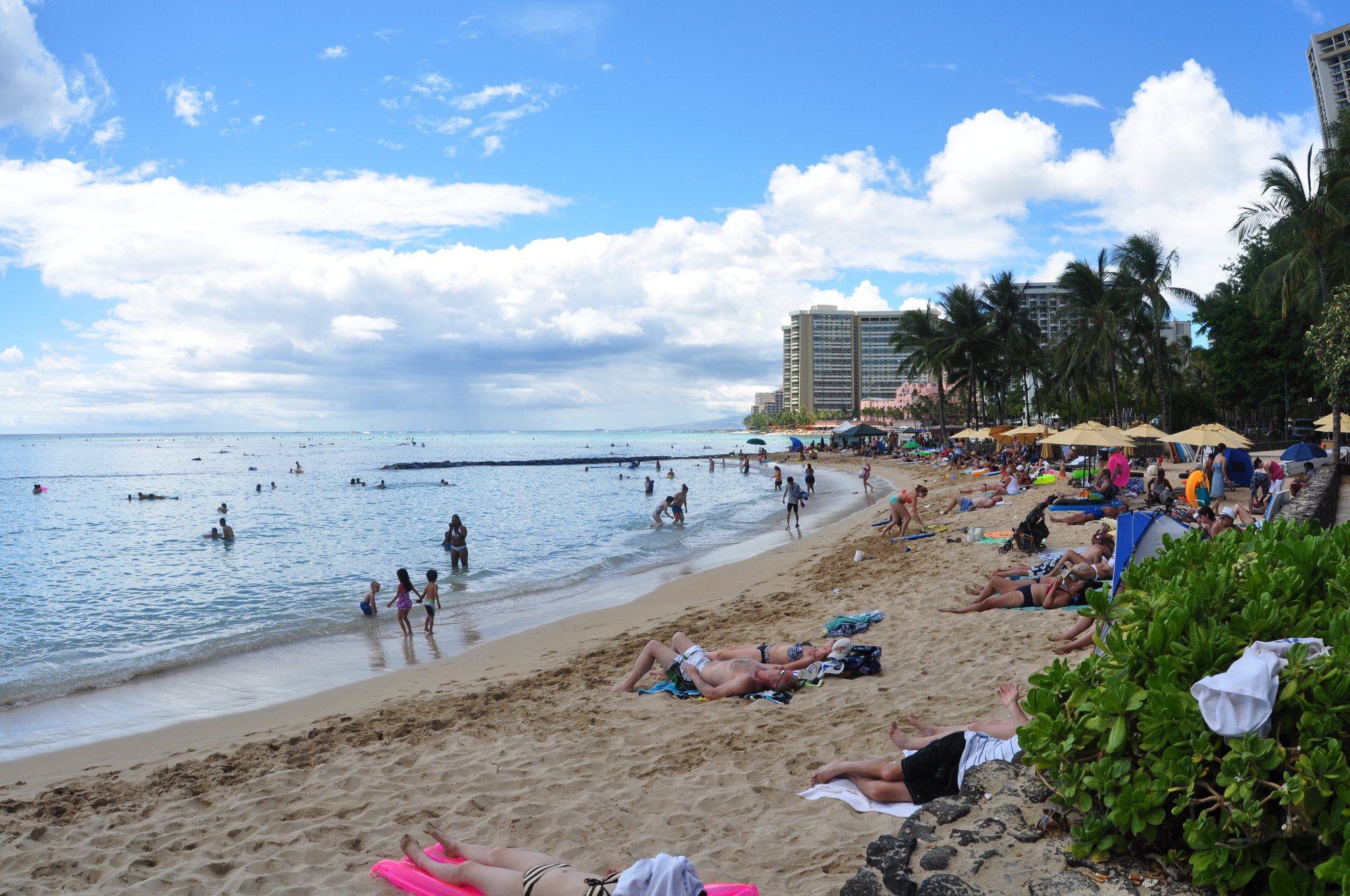 Busy Waikīkī Beach with turquoise water and Honolulu hotel skyline